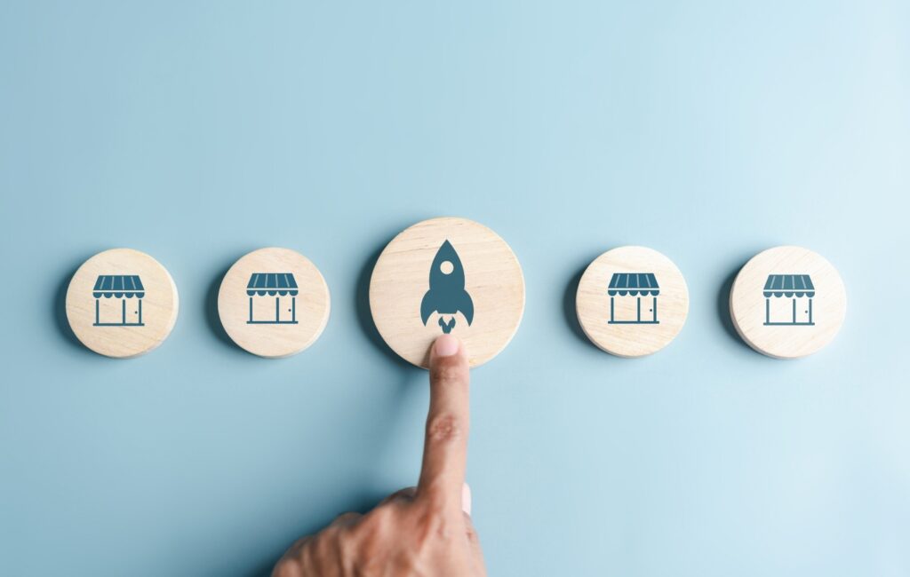 A line of wooden icons showing SaaS products and a finger pointing to the middle one on a blue background.